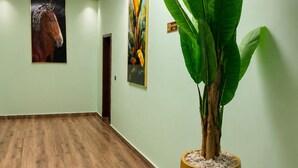 A spacious hallway with wooden flooring, a large potted plant, and two framed artworks on the walls. - LUX PRIMERA HOTEL (Bujumbura)