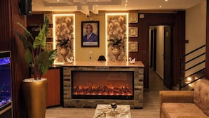 A reception area with a fireplace, a reception desk, a large potted plant, and a modern chandelier. - LUX PRIMERA HOTEL (Bujumbura)