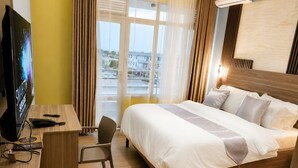 A hotel room with a bed, desk, chair, TV, and a view of the city. - LUX PRIMERA HOTEL (Bujumbura)