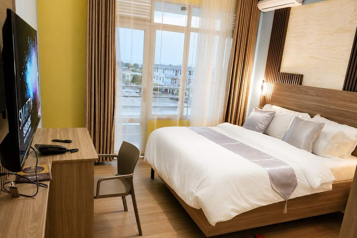 Habitación de hotel con cama, escritorio, silla, televisor y vistas a la ciudad.