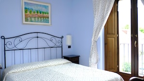 A bedroom with a bed, a nightstand, a wall-mounted lamp, a painting, and a door leading to an outdoor area.