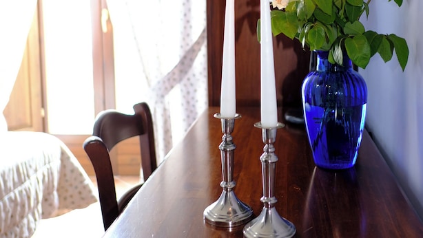 A wooden table with two white candles, a blue vase with green plants, and a lamp.