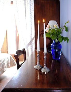Una mesa de madera con dos velas blancas, un florero azul con plantas verdes y una lámpara.