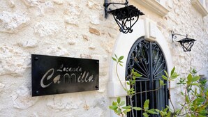 A building with a textured wall, a black sign with white lettering, and a black wrought iron gate.