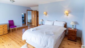 A bedroom with a bed, wooden dresser, chair, bedside tables, and a mirror. - Traditional Cottage in Waterville on the Wild Atlantic Way (Waterville)
