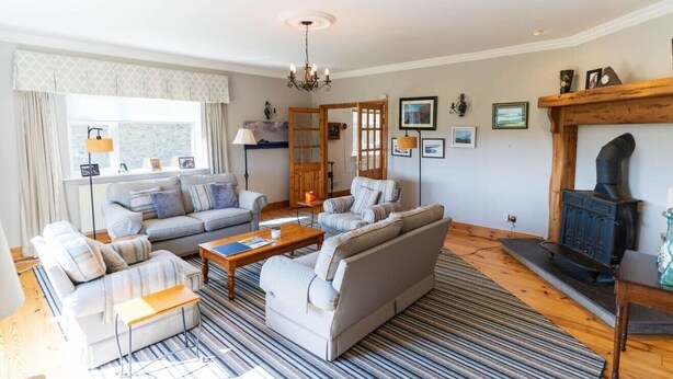 A modern living room with a sofa set, a coffee table, a fireplace, and a large window with curtains. - Traditional Cottage in Waterville on the Wild Atlantic Way (Waterville)