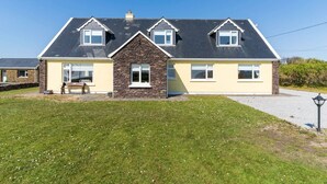 A two-story house with a stone facade, multiple windows, and a paved driveway. - Traditional Cottage in Waterville on the Wild Atlantic Way (Waterville)