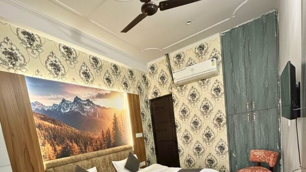 A bedroom with a bed, a ceiling fan, a large window with a mountain view, a wardrobe, and a television. - Hotel Shree Kanha (Jaipur)