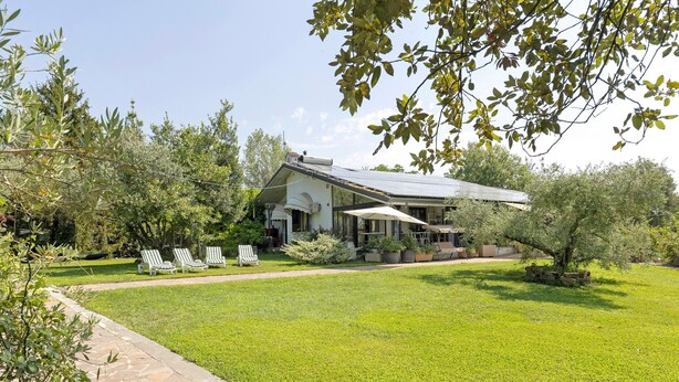 A house with a lawn, white lounge chairs, and a stone pathway.
