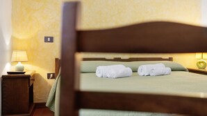 Una cama bien tendida con ropa de cama verde y dos toallas blancas enrolladas, una lámpara de noche y una mesita de noche de madera con una pequeña mesa.