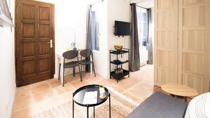 Um quarto com porta de madeira, uma mesa de jantar com cadeiras, uma TV fixada na parede e um guarda-roupa grande.