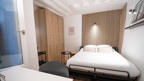 Um quarto com cama, escrivaninha, cadeira, mesa pequena e guarda-roupa.