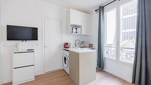 Ett kompakt kök med tvättmaskin, mikrovågsugn, ett litet handfat och en tv som är monterad på väggen.