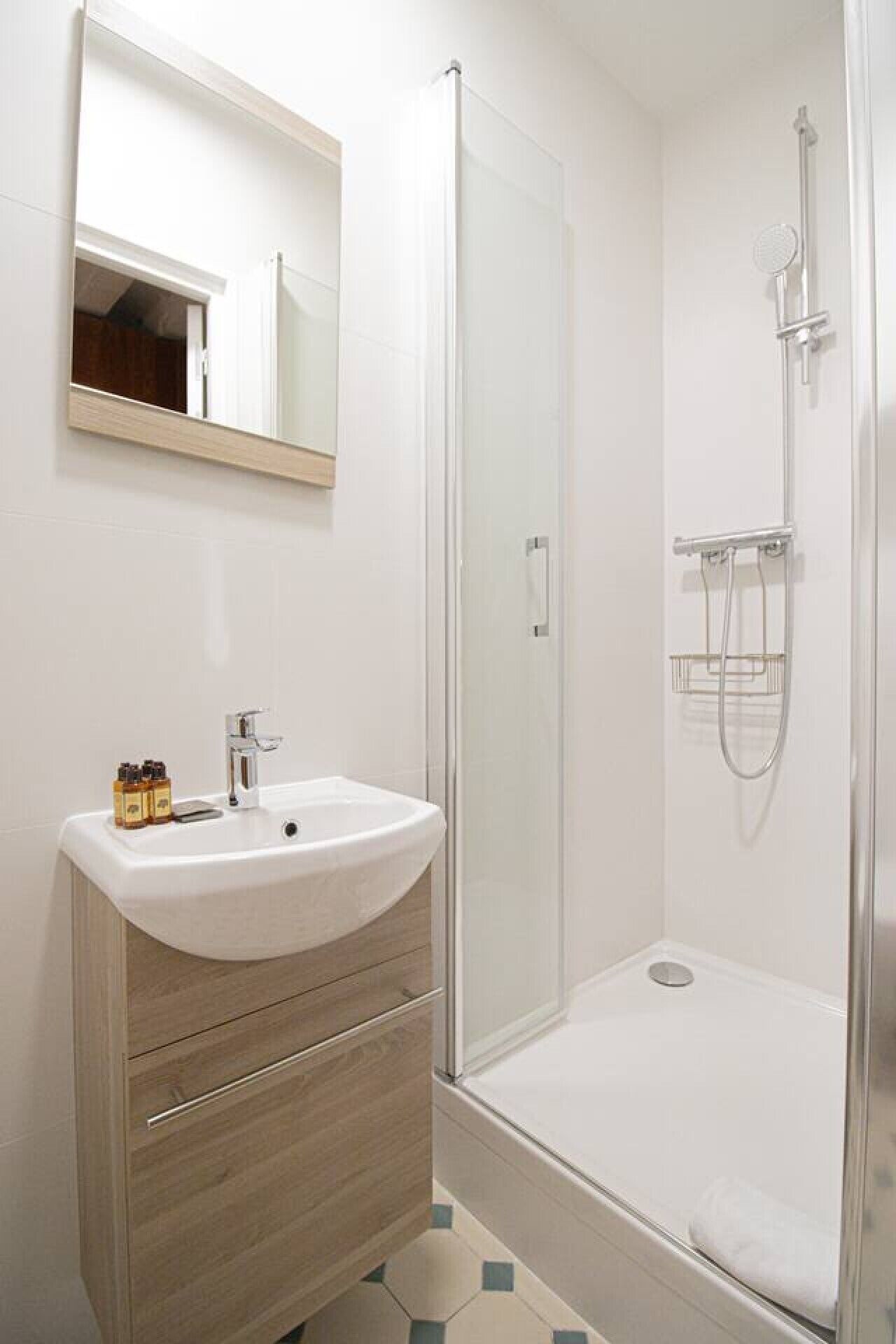 Un bagno moderno con box doccia in vetro, lavabo bianco con mobile in legno e specchio sopra il lavabo.