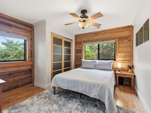 Ein Schlafzimmer mit einem Bett, einem Deckenventilator, einem Fenster, einem Nachttisch und einer Tür mit satinierten Glasscheiben.