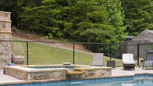 Piscina com degraus de pedra e área cercada, rodeada por vegetação e móveis de exterior.