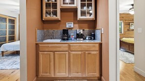 Cozinha compacta com armários de madeira, um espaço para café e uma placa indicando o horário do café.