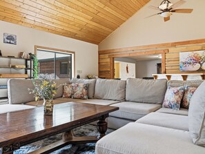 Ein geräumiges Wohnzimmer mit Holzboden, einem großen Ecksofa, einem Holztisch und einem Deckenventilator.
