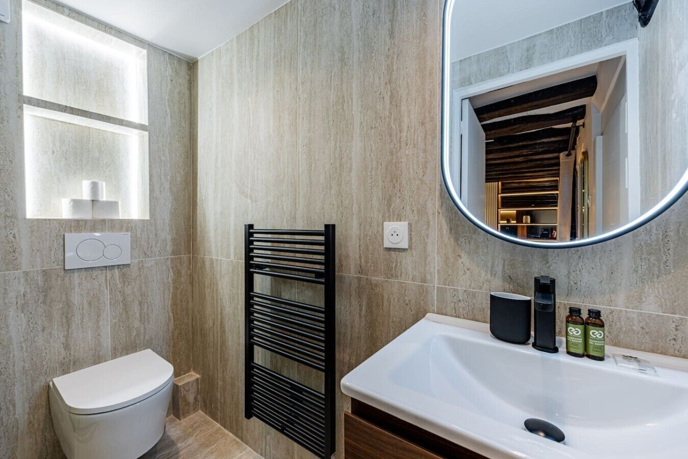Un baño moderno con inodoro, un toallero negro, un espejo grande y un lavamanos con artículos de aseo.