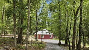 Eine rote Holzhütte in einem Wald, ein Kiesweg führt dorthin.