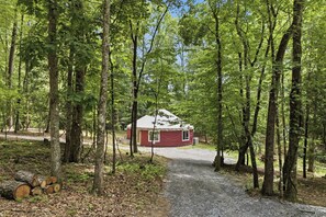 Eine rote Holzhütte in einem Wald, ein Kiesweg führt dorthin.