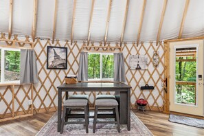 A tented room with a table, two chairs, a window with curtains, a door, and a view of trees. - The Wanderer's Yurt #1 by Chatuge Home Concierge | Luxury Mountain Glamping (Hayesville)