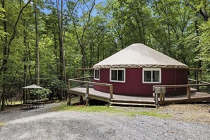 A small, single-story cabin with a red exterior and a white roof, surrounded by a wooden deck and a covered picnic table. - The Wanderer's Yurt #1 by Chatuge Home Concierge | Luxury Mountain Glamping (Hayesville)