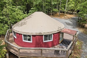 Eine runde, einstöckige Holzhütte mit roter Fassade und beigem Dach, umgeben von einer Holzterrasse und einem Kiesweg.