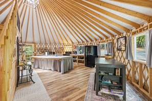 A yurt with a kitchen area, a dining table, and a bookshelf. - The Wanderer's Yurt #1 by Chatuge Home Concierge | Luxury Mountain Glamping (Hayesville)