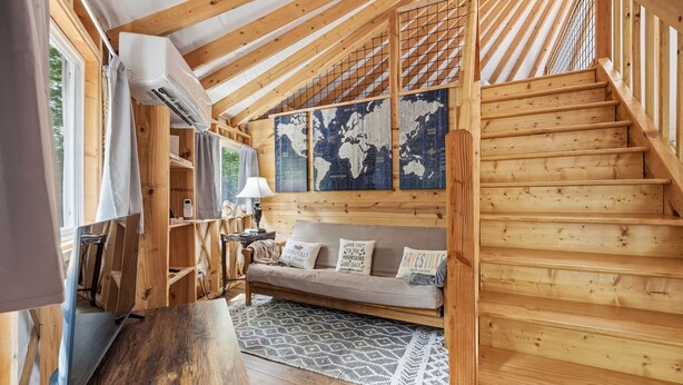 Un interior de madera con una escalera, un sofá, una mesa y un mapa mundial en la pared.