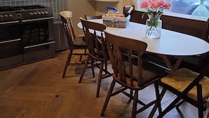 A kitchen with a dining table, chairs, a stove, and a window with a view of the outside. - Escape to Ardchoile | Sleeps 10 with Hot Tub, Log Fire & Games Room (Kingussie)