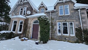 A stone house with a brown door, a satellite dish, and snow on the roof and ground. - Escape to Ardchoile | Sleeps 10 with Hot Tub, Log Fire & Games Room (Kingussie)