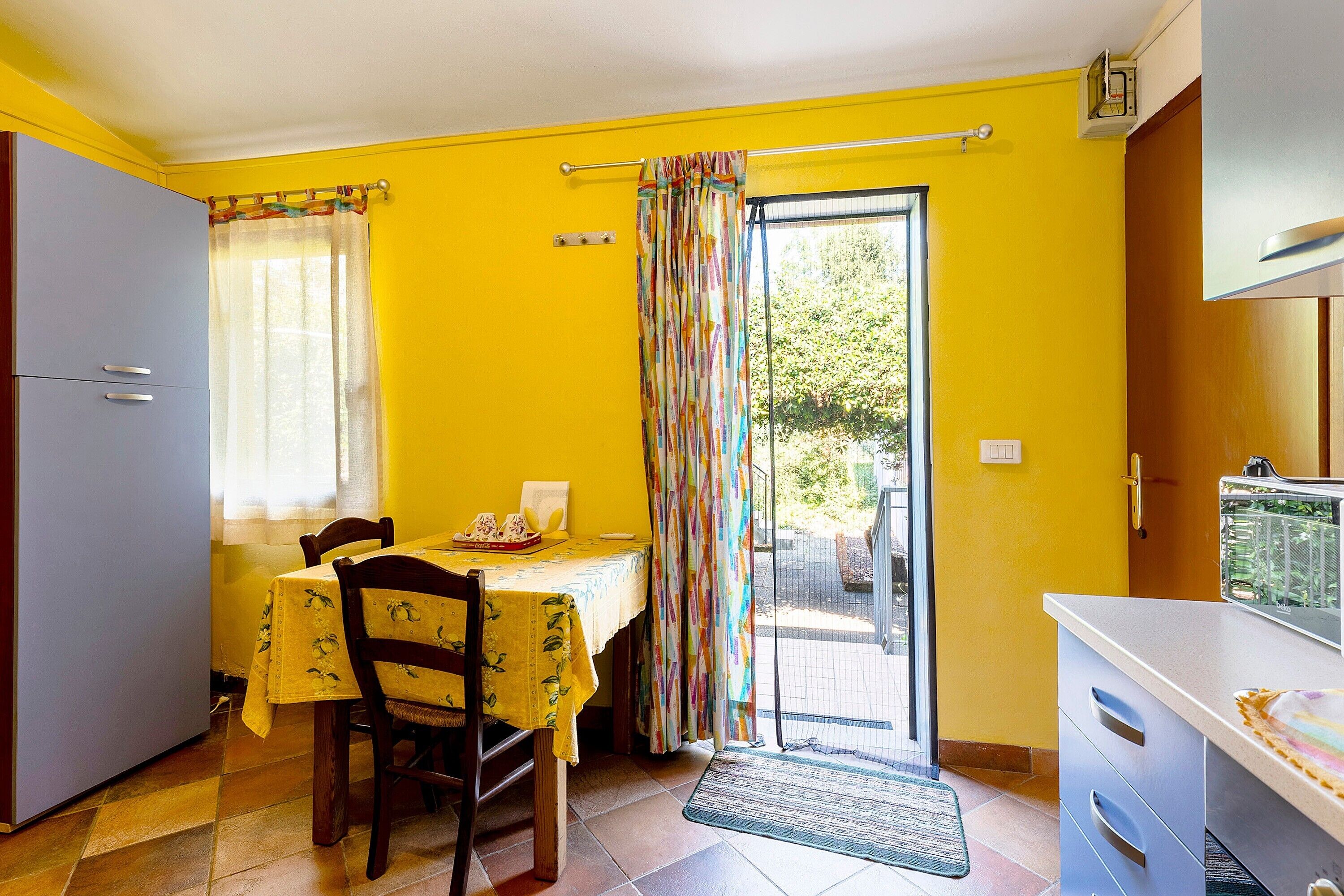 Una habitación con una mesa de comedor, sillas, una cocina y un ventanal corredizo que da a un espacio exterior.