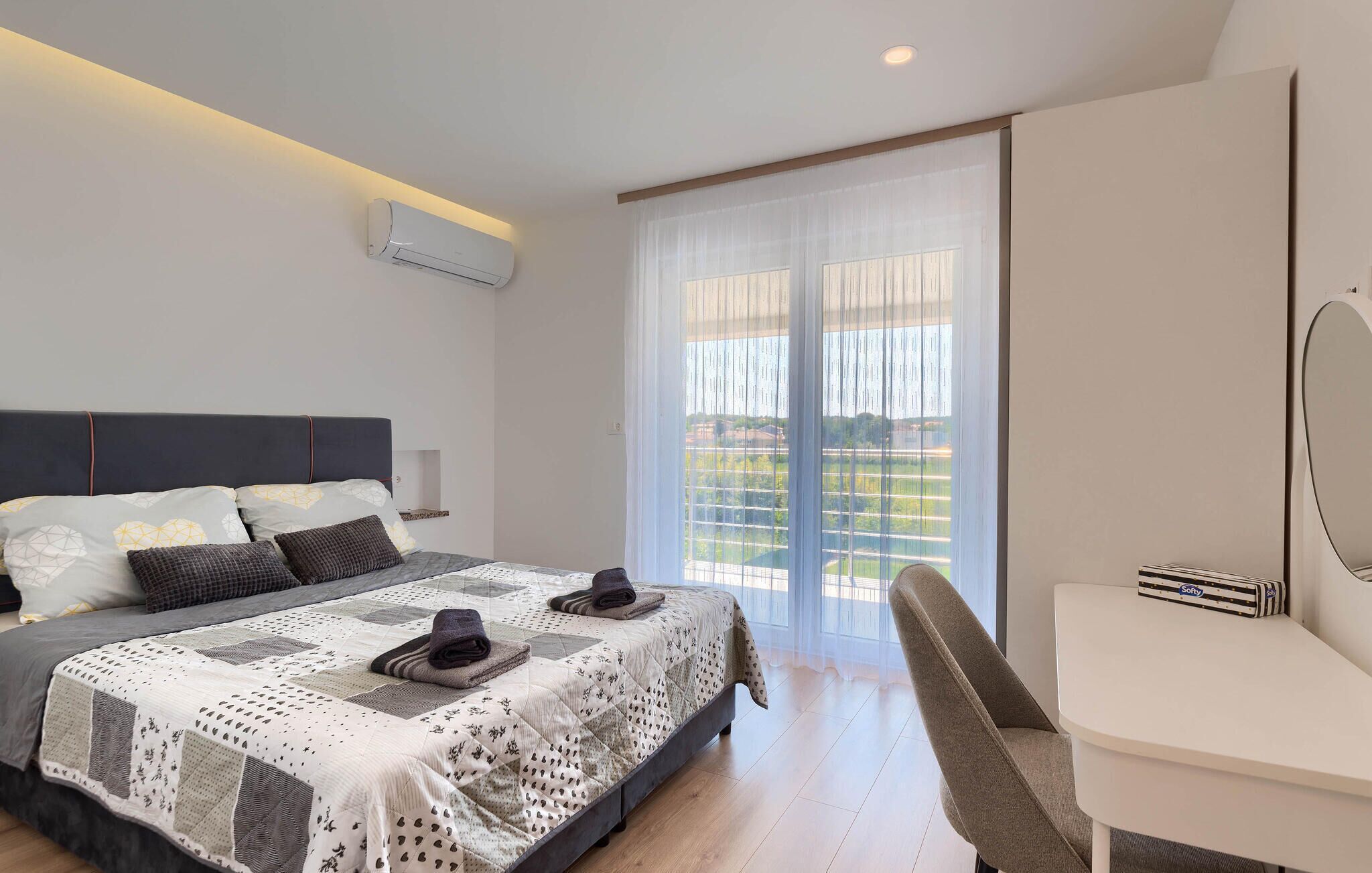 Een moderne slaapkamer met een groot bed, een bureau en uitzicht op een balkon.
