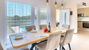 Un comedor con mesa preparada para cuatro personas, ventanas amplias y vista a una piscina.