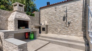 Cocina exterior con horno de piedra, tanque de gas y zona de ducha con manguera.