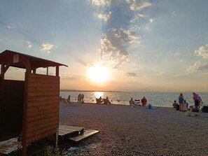 A wooden structure on a pebbled beach with people relaxing and sunbathing. - Oropos Relax View (Oropos)
