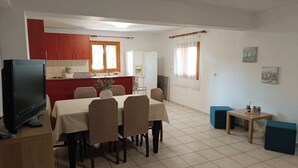 Zona pranzo con tavolo e sedie, televisione e cucina sullo sfondo.