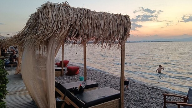 Una zona relax sulla spiaggia con tetto di paglia, terrazza in legno e poltrone da lounge.