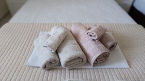 Un letto rifatto con una coperta trapuntata e due set di asciugamani, uno bianco e uno rosa, su un cuscino bianco.