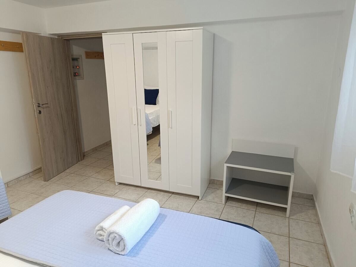 Un dormitorio con una cama, un armario, una mesita y una puerta que da a otra habitación.