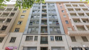 A multi-story residential building with balconies, ground-floor shops, and a visible fire escape. - Regina Margherita by Wonderful Italy (Torino)
