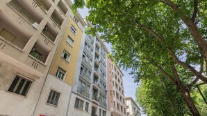 A multi-story building with balconies, a visible storefront with signage, and a tree-lined street. - Regina Margherita by Wonderful Italy (Torino)