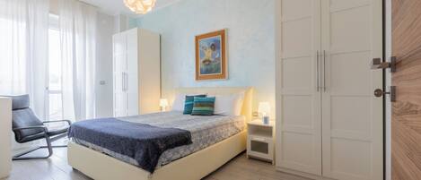 A bedroom with a bed, bedside tables, a chair, a wardrobe, and a painting on the wall.