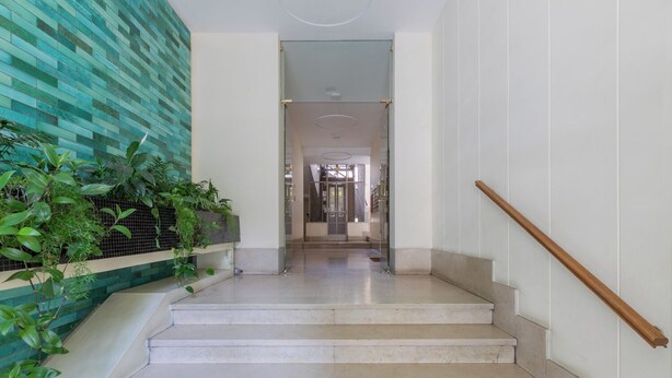A staircase with a wooden handrail, a tiled wall with greenery, and a clear view into a room with a glass door. - Regina Margherita by Wonderful Italy (Torino)