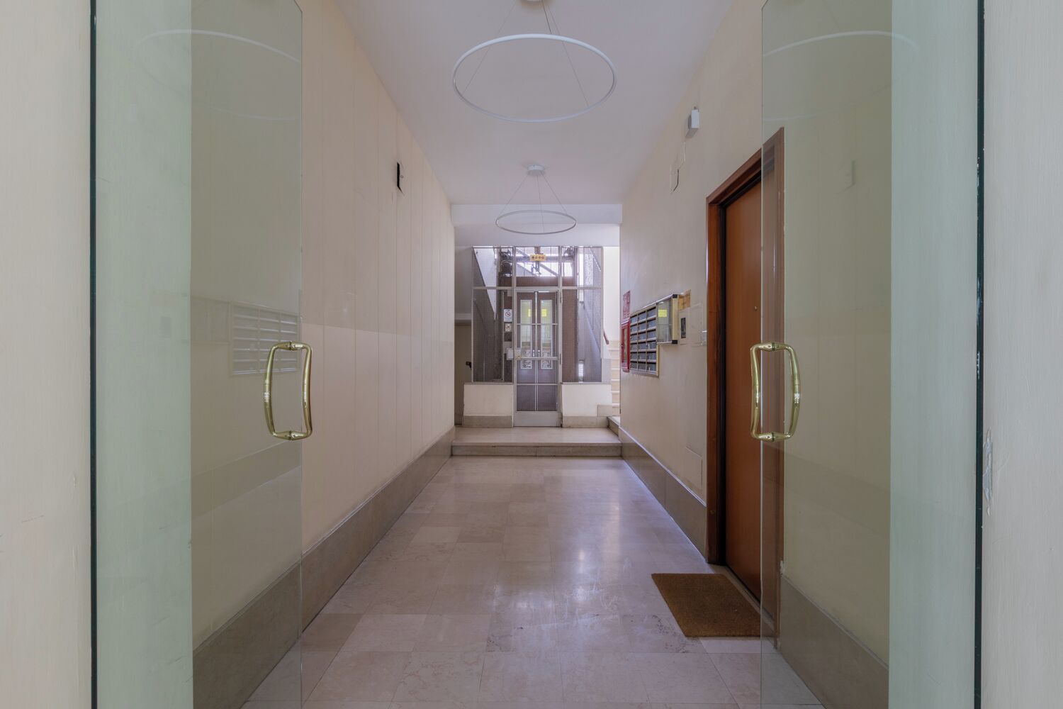 A hallway with glass doors, a wooden door, and a staircase leading to an upper level.
