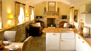 A cozy kitchen with a stone fireplace, wooden counter, and a dining area with a table set for two. - Valley View (Ross-on-Wye)