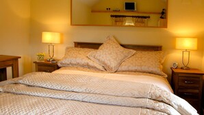 A neatly made bed with a patterned bedspread, two bedside lamps, and a mirror above the headboard. - Valley View (Ross-on-Wye)