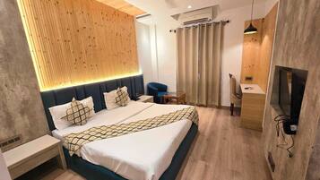 A modern hotel room with a bed, bedside table, TV, and a wooden accent wall.