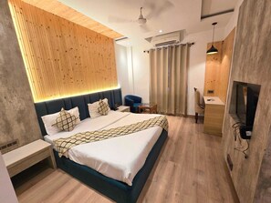 A modern hotel room with a bed, bedside table, TV, and a wooden accent wall.